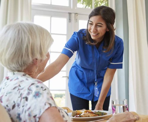 Care nurse serving dinner to a senior woman at home