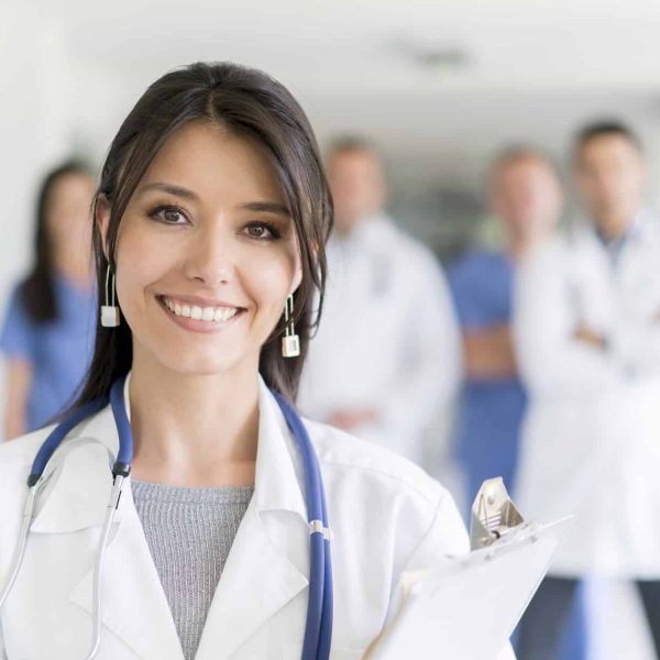 Happy female doctor at the hospital with medical staff at the background looking at the camera and smiling - healthcare and medicine